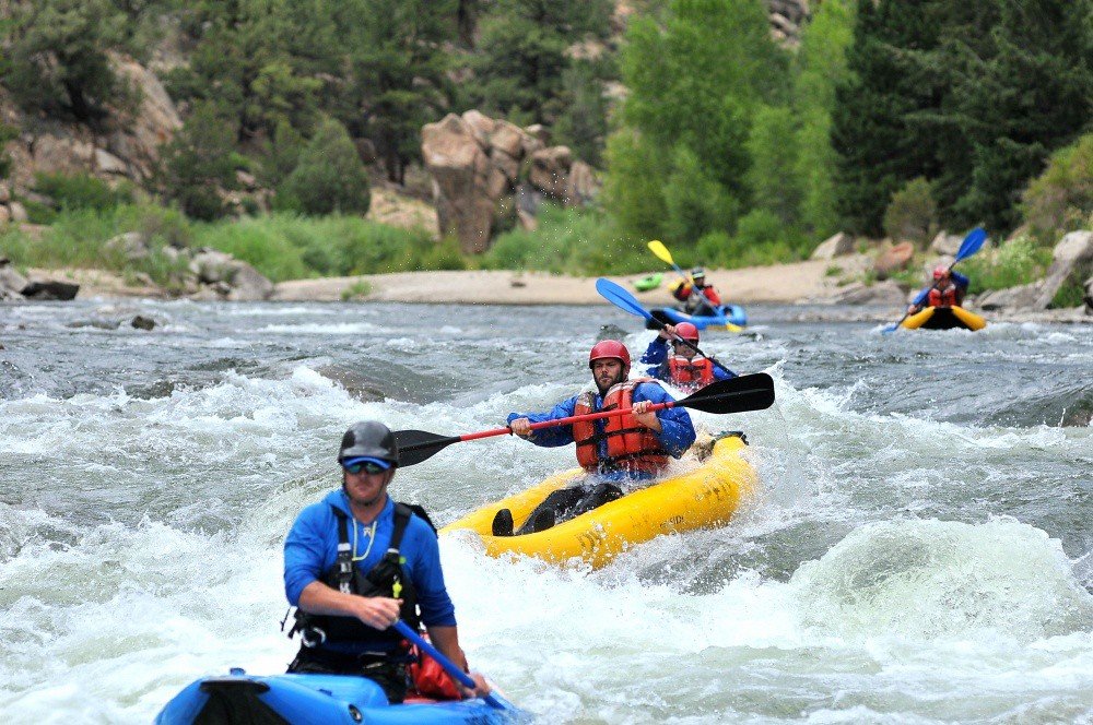 Experience paddling through rapids in the Arkansas River. Lush green scenery surrounds the river. 